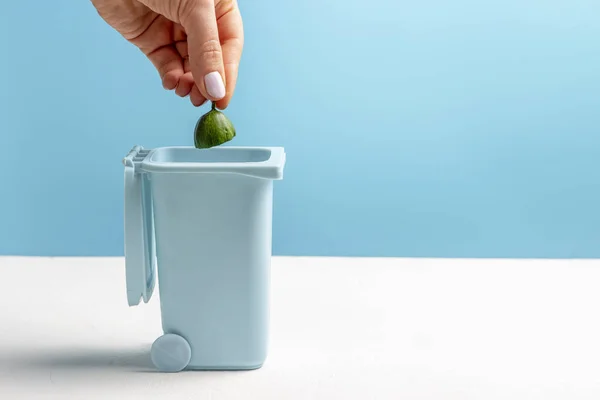 La mano femenina arroja basura de comida en un bote de basura sobre fondo azul y blanco, espacio para copiar — Foto de Stock