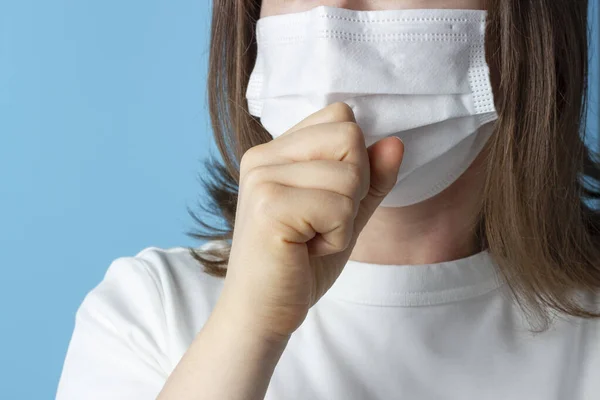 Caucasian Woman in White Mask Coughs on blue background, Concept Cold or Allergy.
