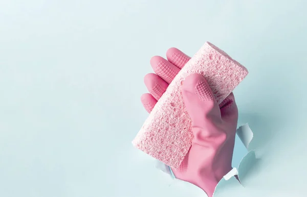 Female hand in pink gloves holds a rag on background of torn blue paper, cleaning service concept