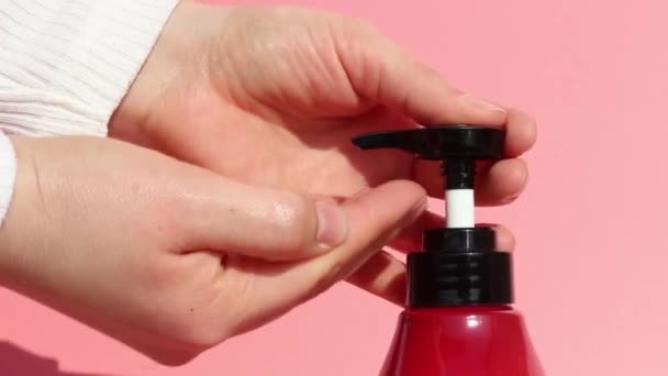 Vrouwelijke handen knijpen zeep met een dispenser close-up, roze achtergrond — Stockvideo