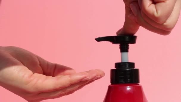 Las manos femeninas exprimen jabón con un dispensador, fondo rosa — Vídeos de Stock