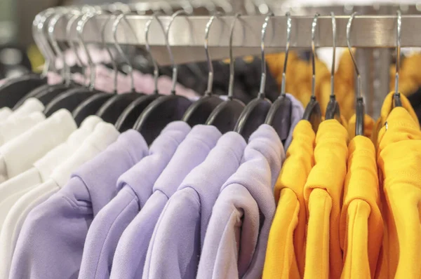 Multicolored sweatshirts hang on a hanger in store close-up. — Stok fotoğraf