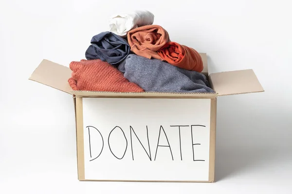 Clothes in cardboard box and the inscription Donate on a white background.