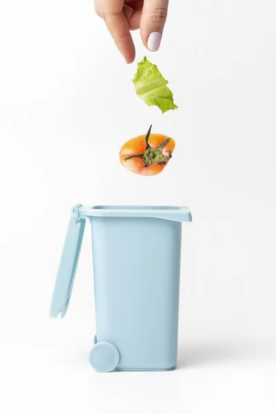 Tangan wanita melempar sampah makanan ke tong sampah, latar belakang putih — Stok Foto
