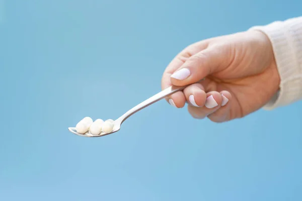 Hand hält einen Löffel mit weißen Kollagenkapseln auf blauem Hintergrund. — Stockfoto