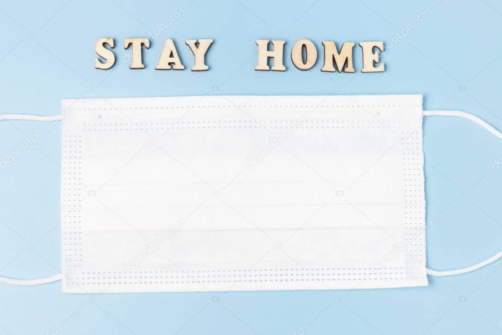 Stay home inscription and white mask, blue background top view, copy space