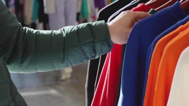 Egy férfi pulóvert választ, ami egy vállfán lóg egy ruhaboltban.. — Stock videók