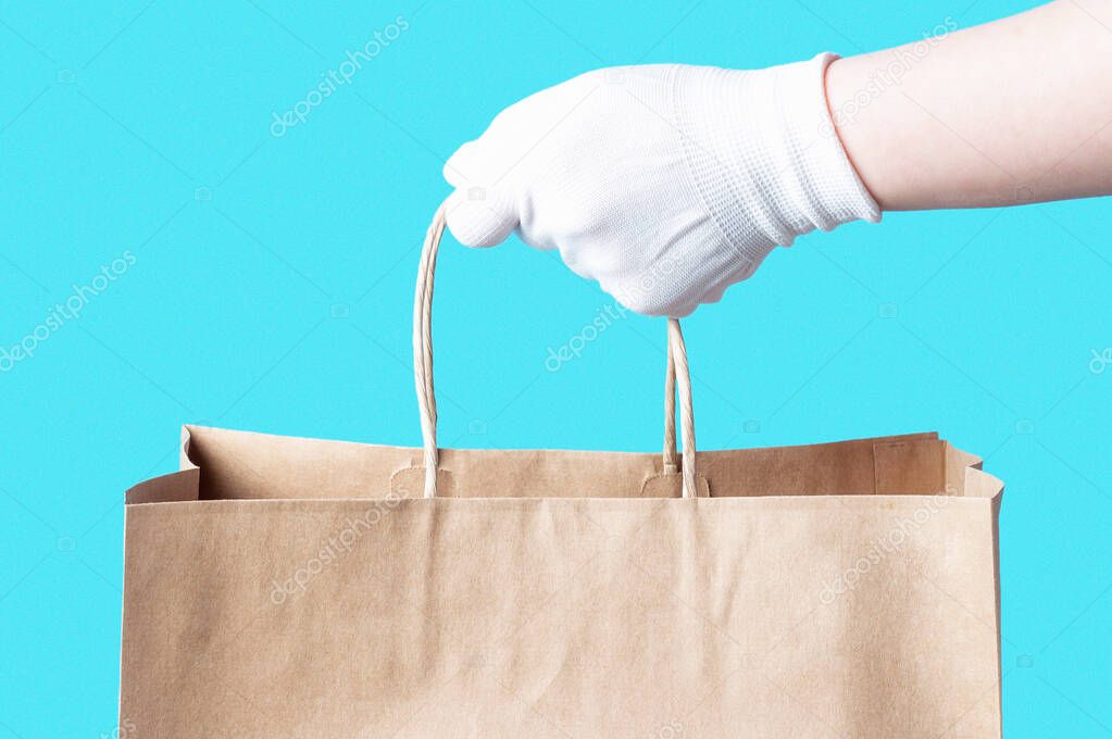 Female hand in a white glove holds a brown cardboard bag, food delivery concept.