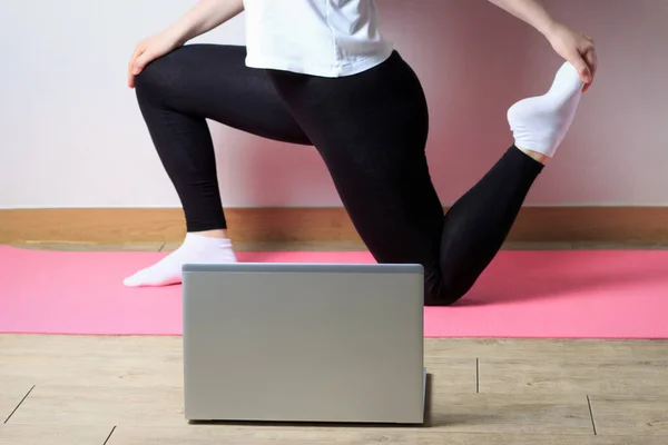 The girl in sporting black pants and white shirt makes a stretch in front of the laptop