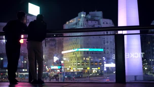 Dos hombres charlando y disfrutando de la vista del monumento al Obelisco por la noche — Vídeo de stock