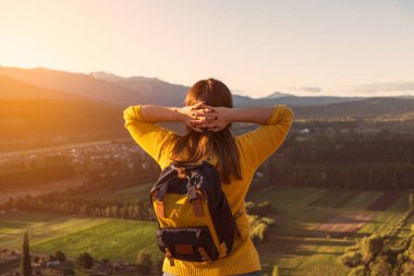Rahatlamış genç bir kadın kolları boynunun arkasında manzaraya bakıyor.