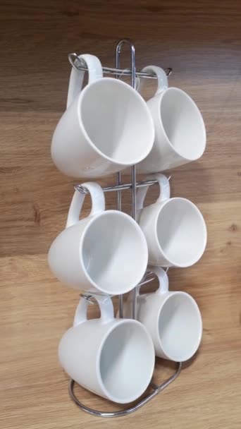 Six empty large white ceramic cups hanging on stand,swaying from side to side, against the background of wooden kitchen panels. Concept of invitation for coffee. Modern design, minimalism. Vertical — Stock Video