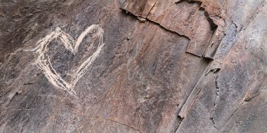 Kalp kabaca bir kayaya çizilmiş. Kabataslak kabartma. Aşk ilanı. Kendi ellerinle yaptın. Dürtüsel duygu ve duygu ifadesi kavramı. Sevgililer Günü Acımasız kartpostal tasarımı
