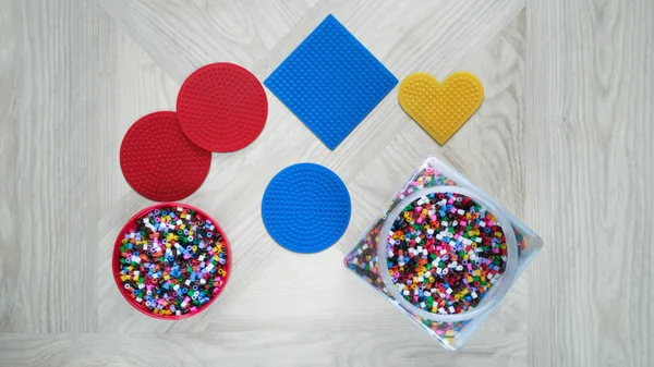 Step-by-step instructions for thermo mosaic: step 1.Set of several circle,square and heart-shaped forms with pins,jar and container lid with beads.Concept of quiet family game with children at home