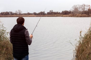 Sisli bir sisli gündoğumunda, nehir kıyısında dönen bir çubukla balık tutan bir adam.