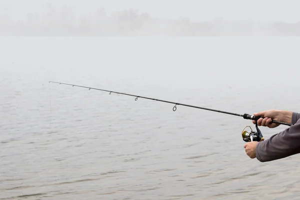 Las manos de un pescador con una varilla de hilar y bobina mañana de verano en el lago —  Fotos de Stock