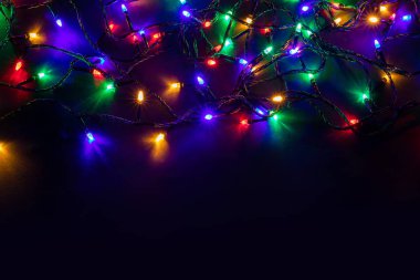 Işıklı ve bedava metin alanlı bir Noel arkaplanı. Noel ışıkları sınırda. Siyah arka planda parıldayan renkli Noel ışıkları. Yeni yıl. Noel zamanı. Dekorasyon. Çelenk.