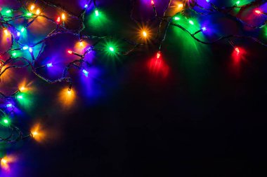 Işıklı ve bedava metin alanlı bir Noel arkaplanı. Noel ışıkları sınırda. Siyah arka planda parıldayan renkli Noel ışıkları. Yeni yıl. Noel zamanı. Dekorasyon. Çelenk.