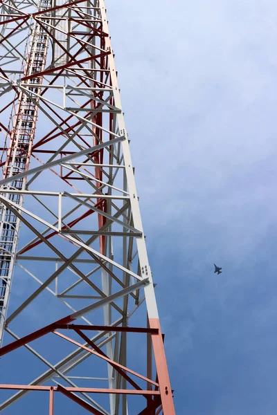 The telephone tower is white and red. View from bottom to top. Sky and airplane is background.