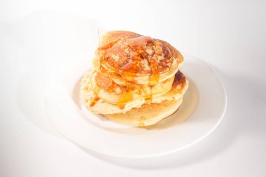 Krepler beyaz bir tabağa istiflenmiş, krepler balla kaplanmış.