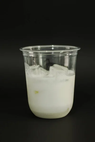 Milk and ice cubes in a plastic glass on a black background