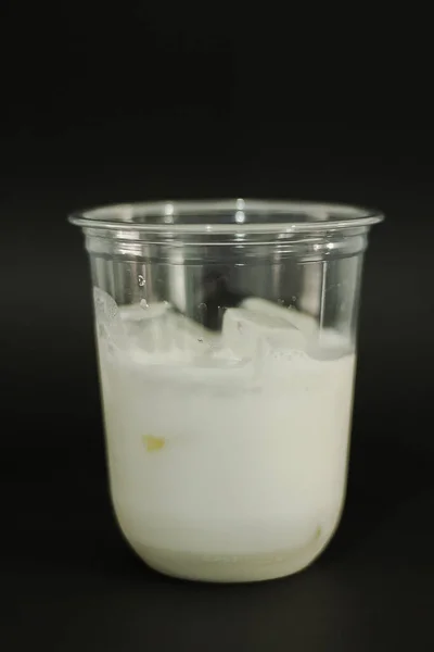 Milk and ice cubes in a plastic glass on a black background