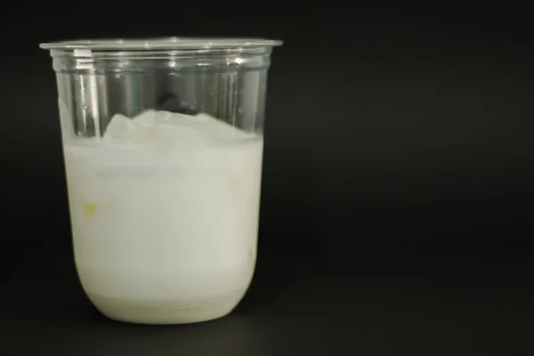 Milk and ice cubes in a plastic glass on a black background