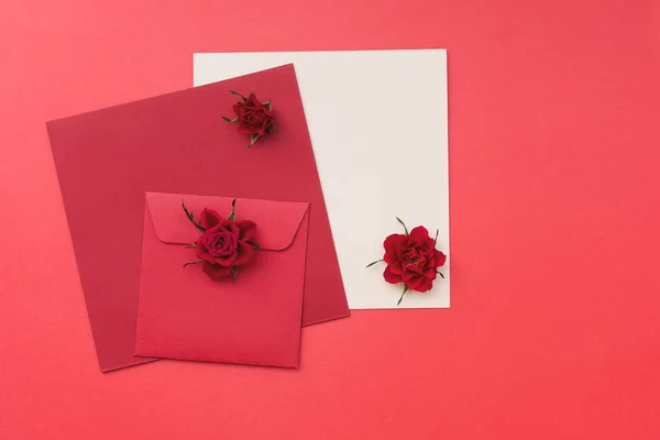 Rosas rojas con una tarjeta de felicitación en blanco y sobre sobre fondo de papel rojo — Foto de Stock