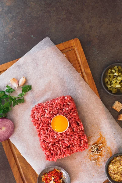 Färsk köttfärs, äggula och andra ingredienser på rustika bakgrund — Stockfoto