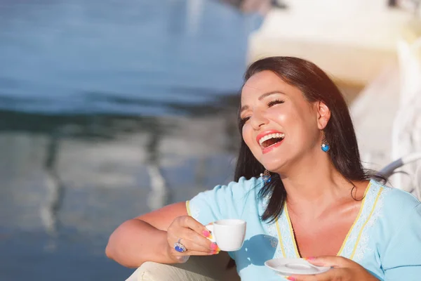 Прекрасная счастливая женщина пьет кофе на пирсе на закате — стоковое фото