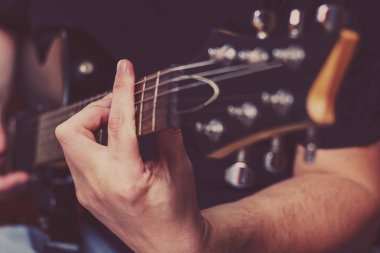 Closeup el parmaklarıyla sadece odakta siyah bir arka plan üzerinde elektrik gitar çalmak bir adam