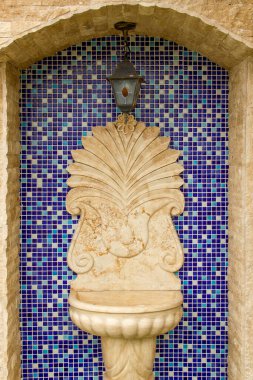 Modern yapı malzemeleriyle yapılmış antika bir lavabo. Arka planda mavi bir mozaik var.