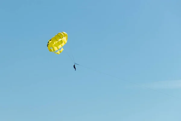 Parasailing είναι μια ενεργή μορφή αναψυχής. Ένα κίτρινο αλεξίπτωτο πετάει στον γαλάζιο ουρανό μαζί με χαρούμενους τουρίστες από το τοπίο από ψηλά — Φωτογραφία Αρχείου