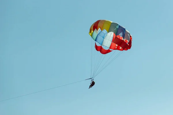 Mit einem Fallschirm zum Fallschirmspringen fliegt ein Paar durch die Luft mit blauem Himmel im Hintergrund. — Stockfoto