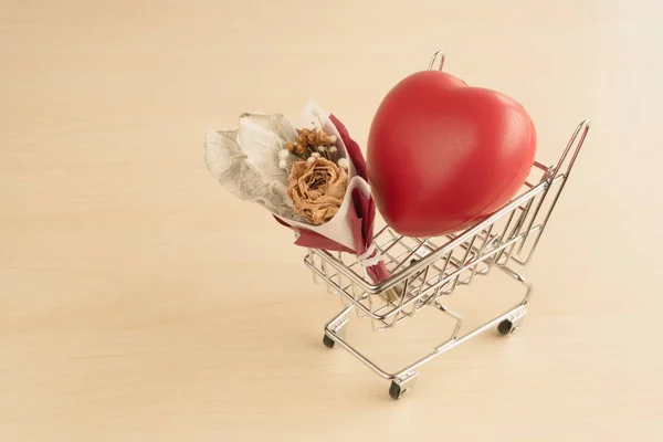 Red love heart and dried flower bouquet in shopping cart on wood table