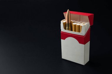 Sigara öldürür kavramı, koyu arka plan üzerinde sigara paketindeki bir silah mermi