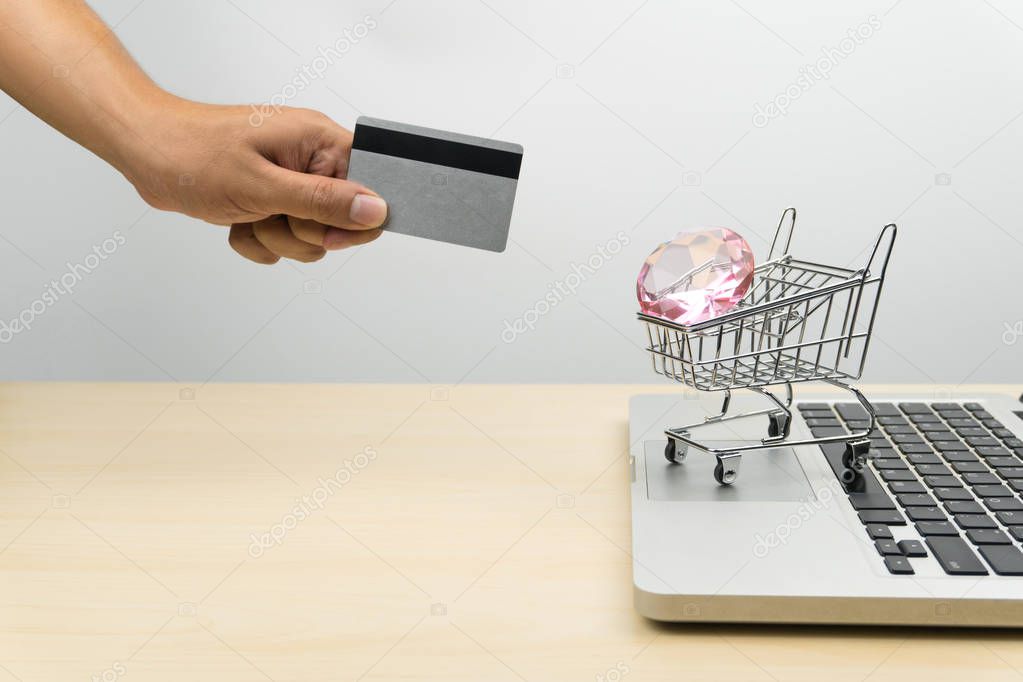 hand holding credit card, a diamond in a shopping cart on a laptop, online shopping concept