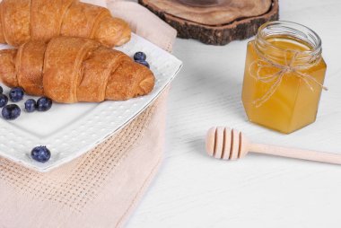 Beyaz tabakta yaban mersinli kruvasan, kahve ve bal. Lezzetli bir kahvaltı. Kapat.