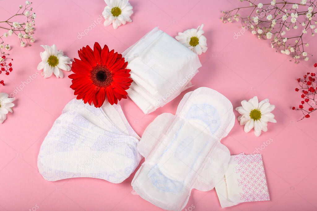 Lot of menstrual pads with red gerbera and white camomile on pink girlish background, top view, copy space. Ovulation concept. menstruation concept.