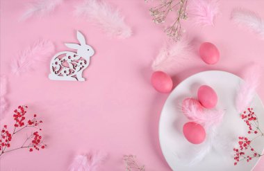 Mutlu Paskalyalar. Paskalya arkaplanını tebrik ederim. Paskalya yumurtaları, beyaz tabakta pastel pembe tüylerle süslenmiş paskalya tavşanı. Moda konsepti. Üst görünüm, düz görünüm, model