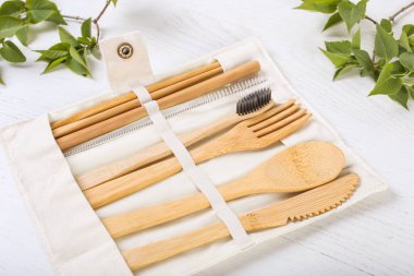 Tahta beyaz arka planda bir çanta içinde çevre dostu bambu çatal bıçak takımı. Sürdürülebilir yaşam tarzı. Plastiksiz konsept. Kapat.