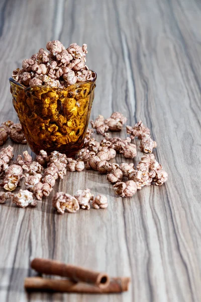 Pipoca de aroma de chocolate no vidro amarelo e na mesa de madeira marrom com canela e fundo de flor branca — Fotografia de Stock