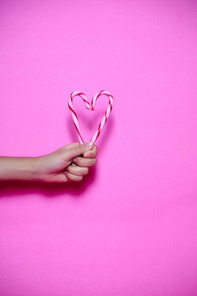 Женщины держат в руках леденцы в форме сердца на розовом фоне
