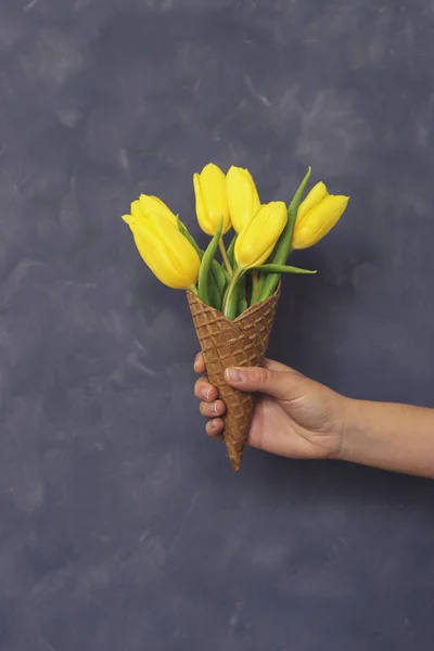 Yellow tulips in ice cream cone in girls hand on cement backgrou