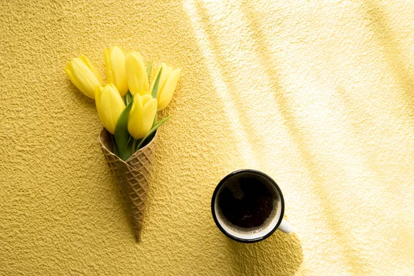 Tulips in ice cream cone on yellow background