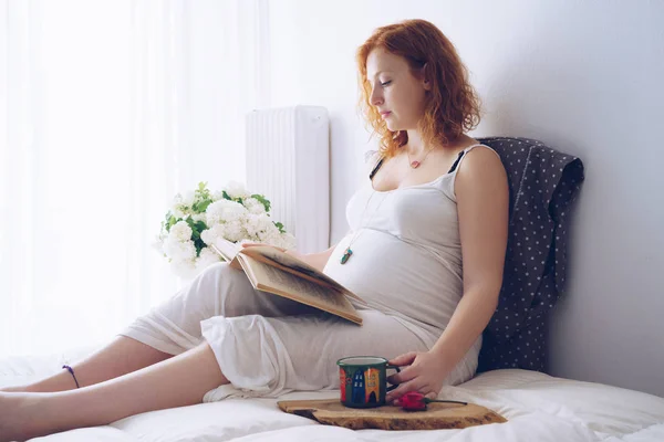 Młoda kobieta w ciąży, relaks na łóżku z książką — Zdjęcie stockowe