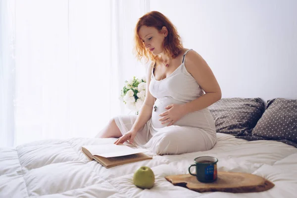 Fiatal terhes nő pihentető egy könyvet az ágyon — Stock Fotó