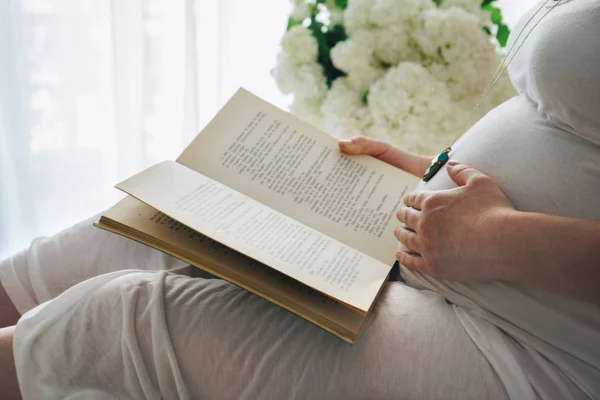 Schwangere berührt ihren Bauch, während sie ein Buch liest — Stockfoto