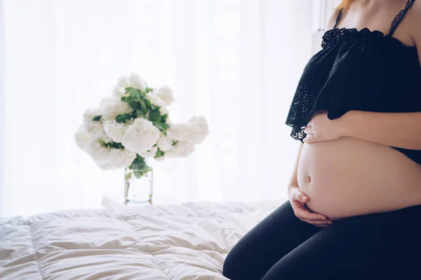 Zwangere vrouw zitten in bed en haar buik met handen aan te raken — Stockfoto