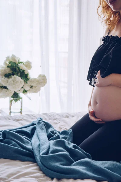 Kobieta w ciąży, siedząc na łóżku i dotykając jej brzuch rękami — Zdjęcie stockowe